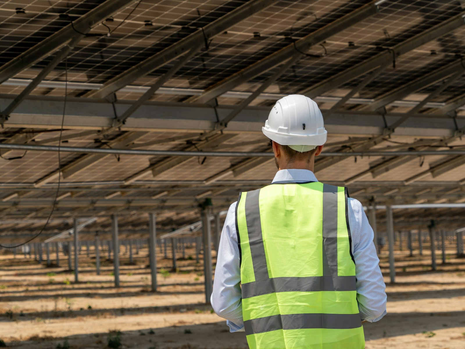 Solar field professional wearing high-visibility safety equipment beneath photovoltaic arrays